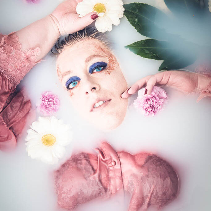 Portraitiste - Portrait d'une femme ronde dans un bain de lait au milieu de fleurs rose et blanche